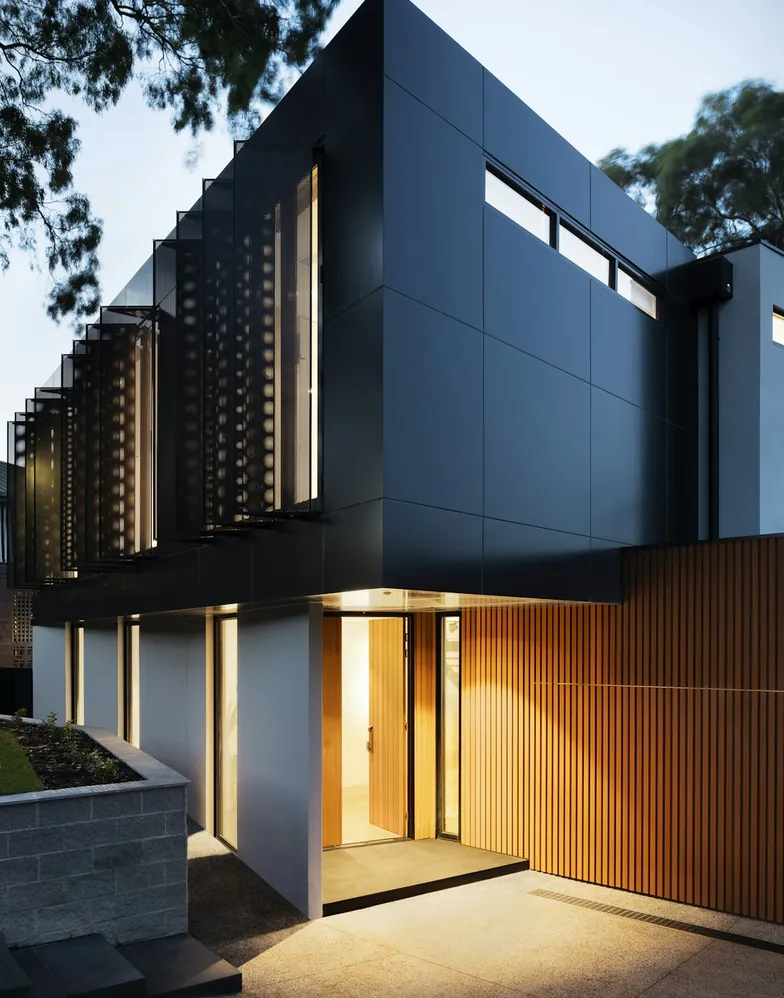 A timber-clad residential building with warm lit interiors