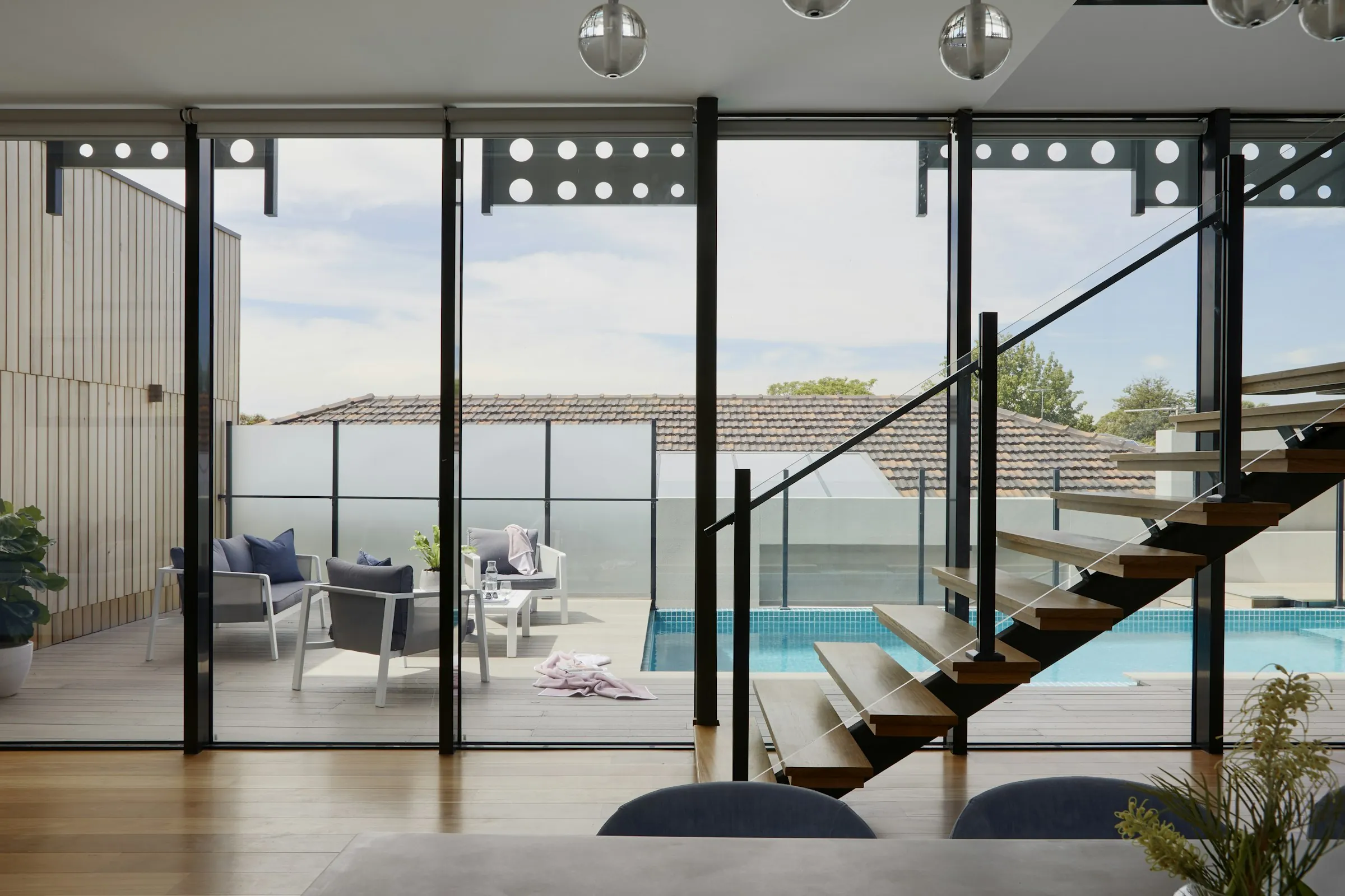 A glass-walled living room opening onto a pool and the bay beyond